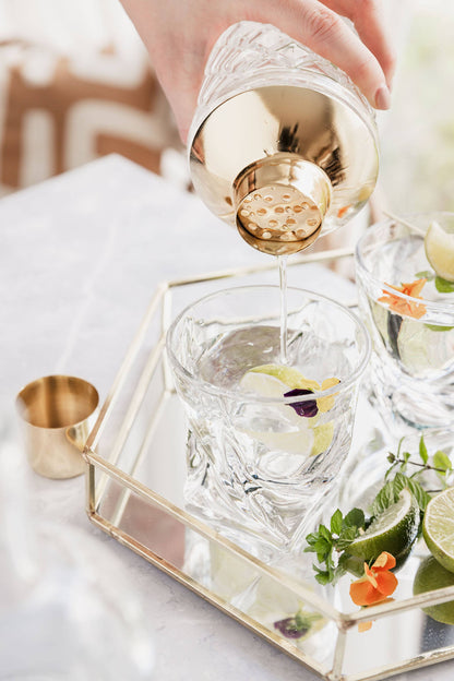 Close up of hand pouring a cocktail using large cut glass cocktail shaker with gold colour top by Uberstar