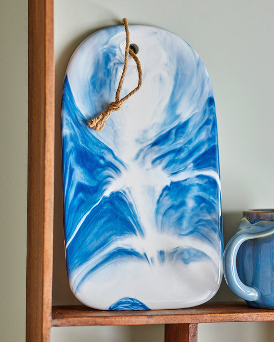 Blue and white marbled cutting board hanging on a wooden shelf.