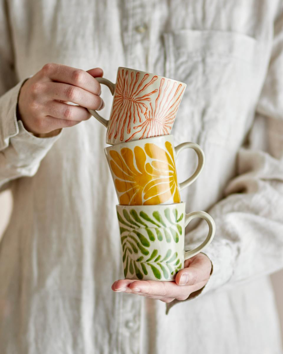 Stack of colorful ceramic mugs held by a person against a neutral background
