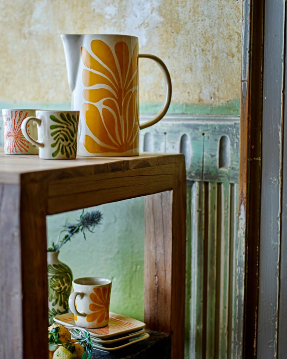 Decorative mugs with sunflower design on a wooden surface with a vintage-style wall in the background.