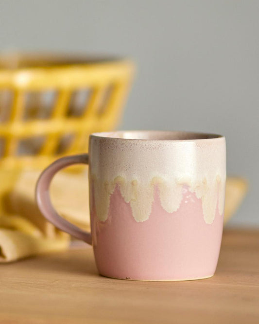 Pink ceramic mug with a textured design on a wooden surface with a blurred yellow basket in the background.