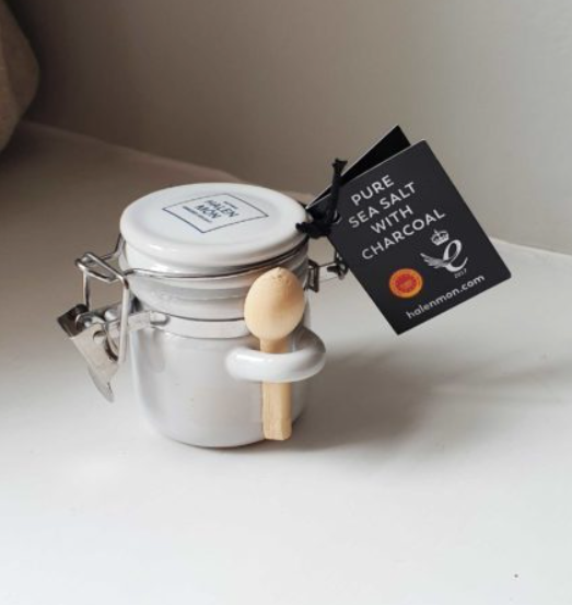 Small white ceramic jar with wooden spoon attached, containing pure sea salt with charcoal by brand Halen Môn