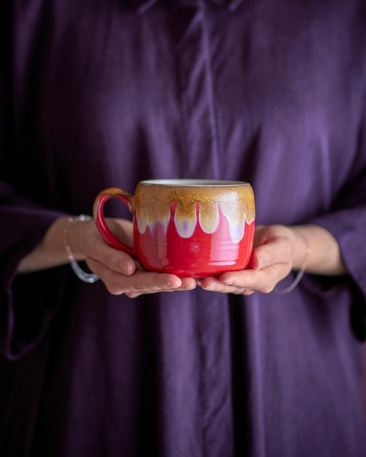 Person holding a red mug with artistic design against a purple background