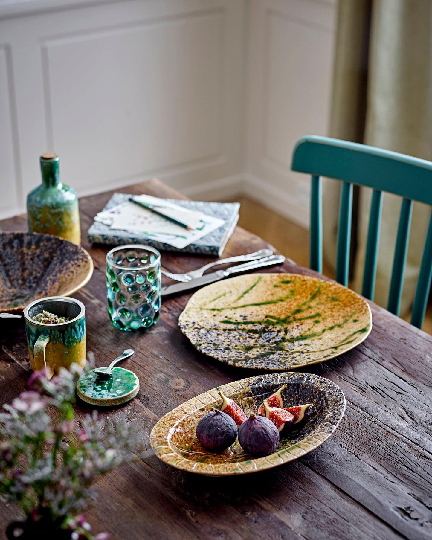 Dining table with ceramic plates, glasses, and utensils on a wooden surface.
