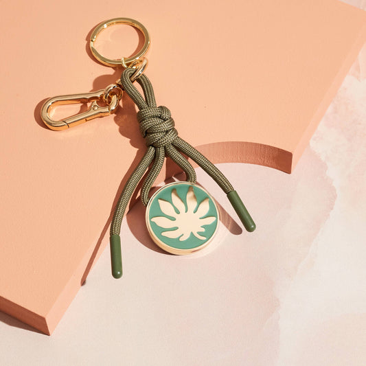Bag charm keychain with green rope and circular leaf charm in gold on green.