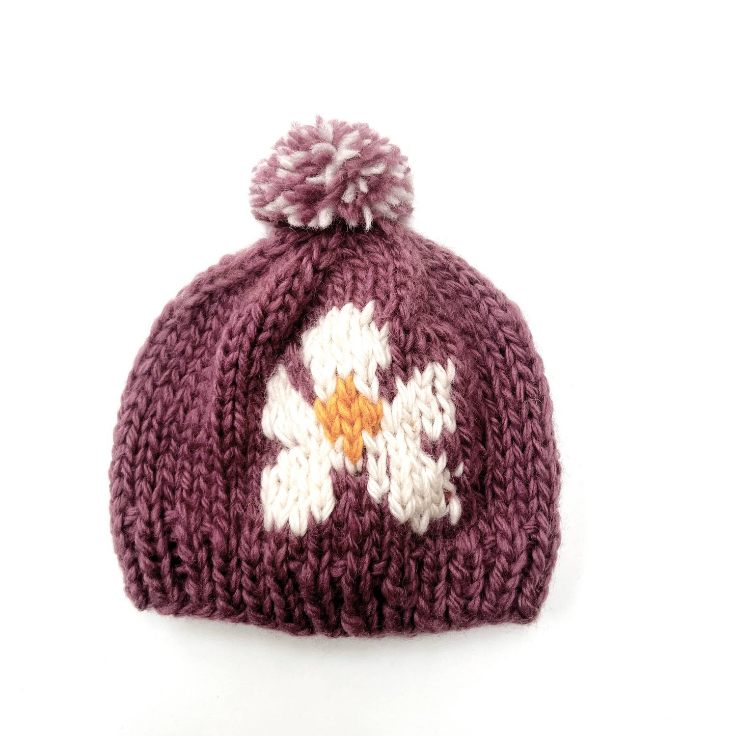 Thick, chunky woollen baby winter hat, by Pebble Child, made from 100% New Zealand merino wool in plum colour with a white flower and a pompom on top.
