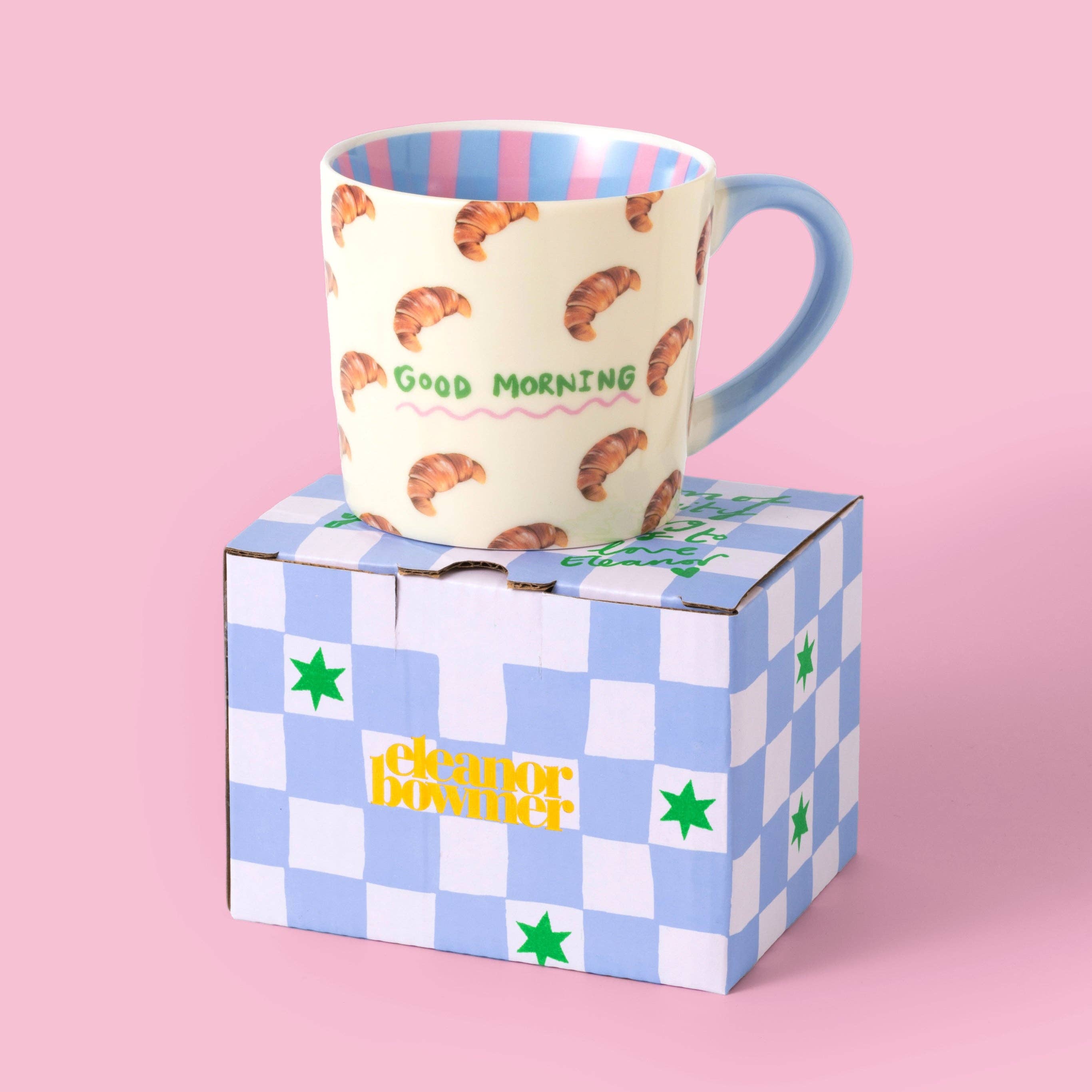 Mug with croissant pattern and 'Good Morning' text by Eleanor Bowmer, on top of blue and white check gift box.