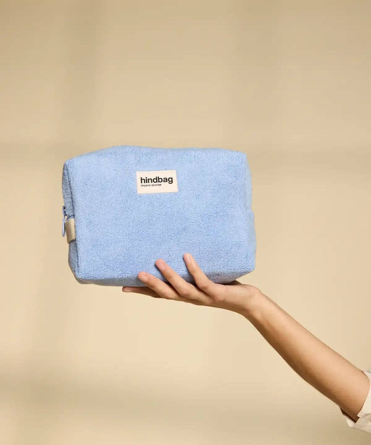 Hand holding a blue pouch with 'hindbag' label against a beige background