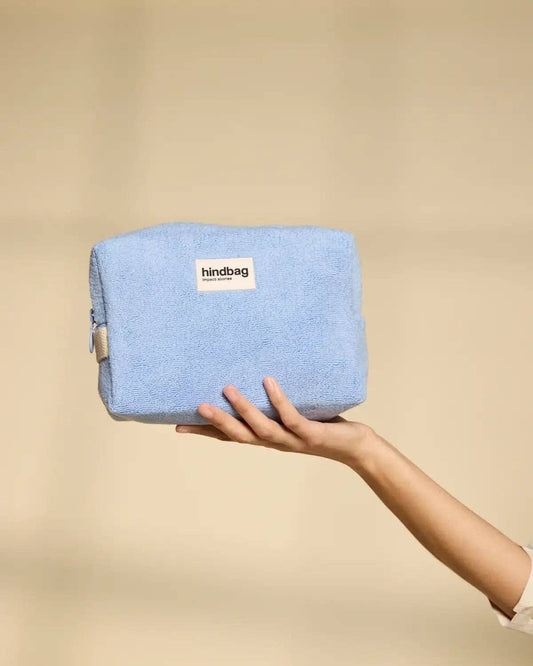 Hand holding a blue pouch with 'hindbag' label against a beige background
