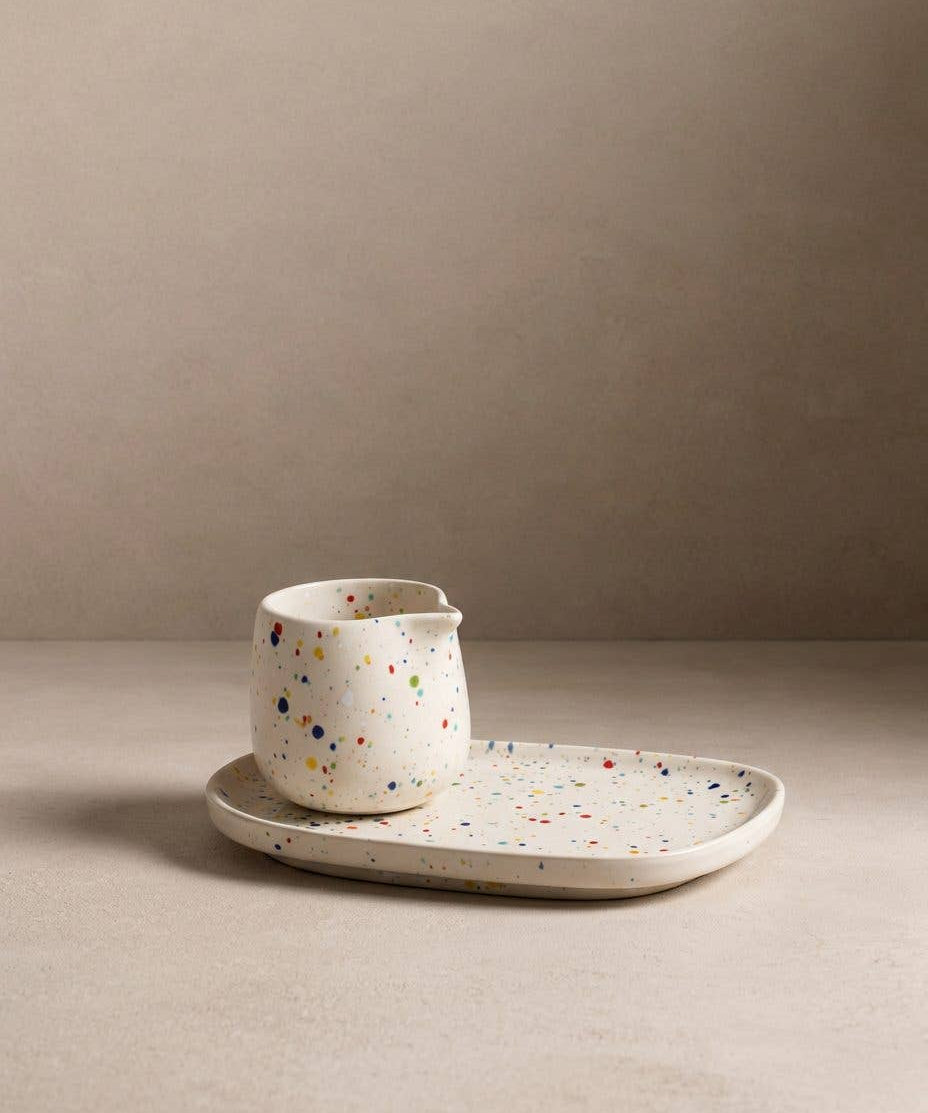 Egg Back Home white ceramic jug with multicoloured speckles on a tray against a beige background