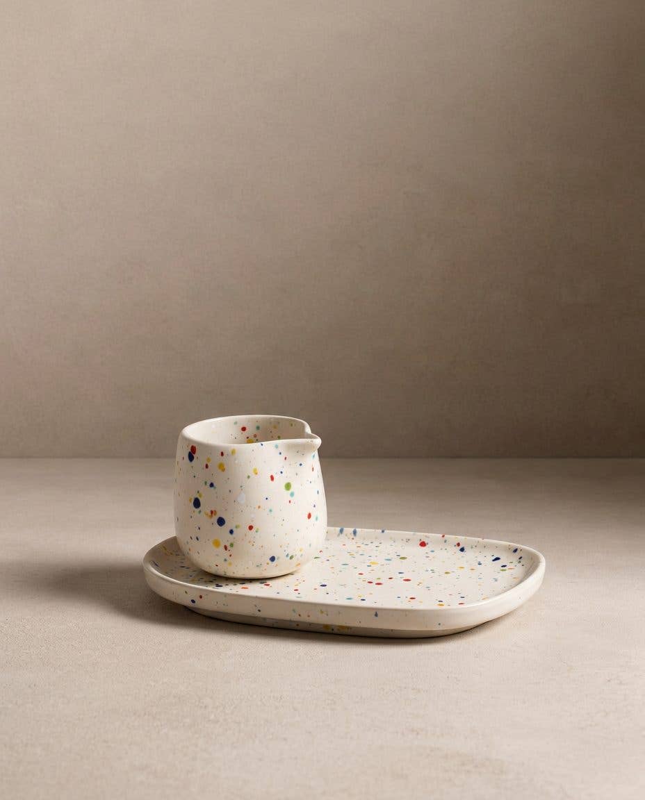Egg Back Home white ceramic jug with multicoloured speckles on a tray against a beige background