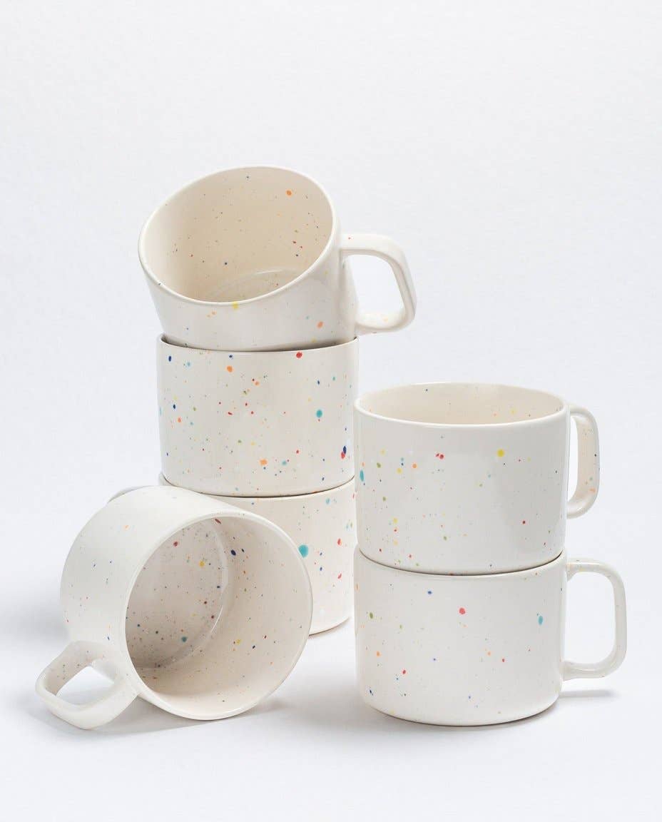 Set of white ceramic mugs with colorful speckles on a light gray background