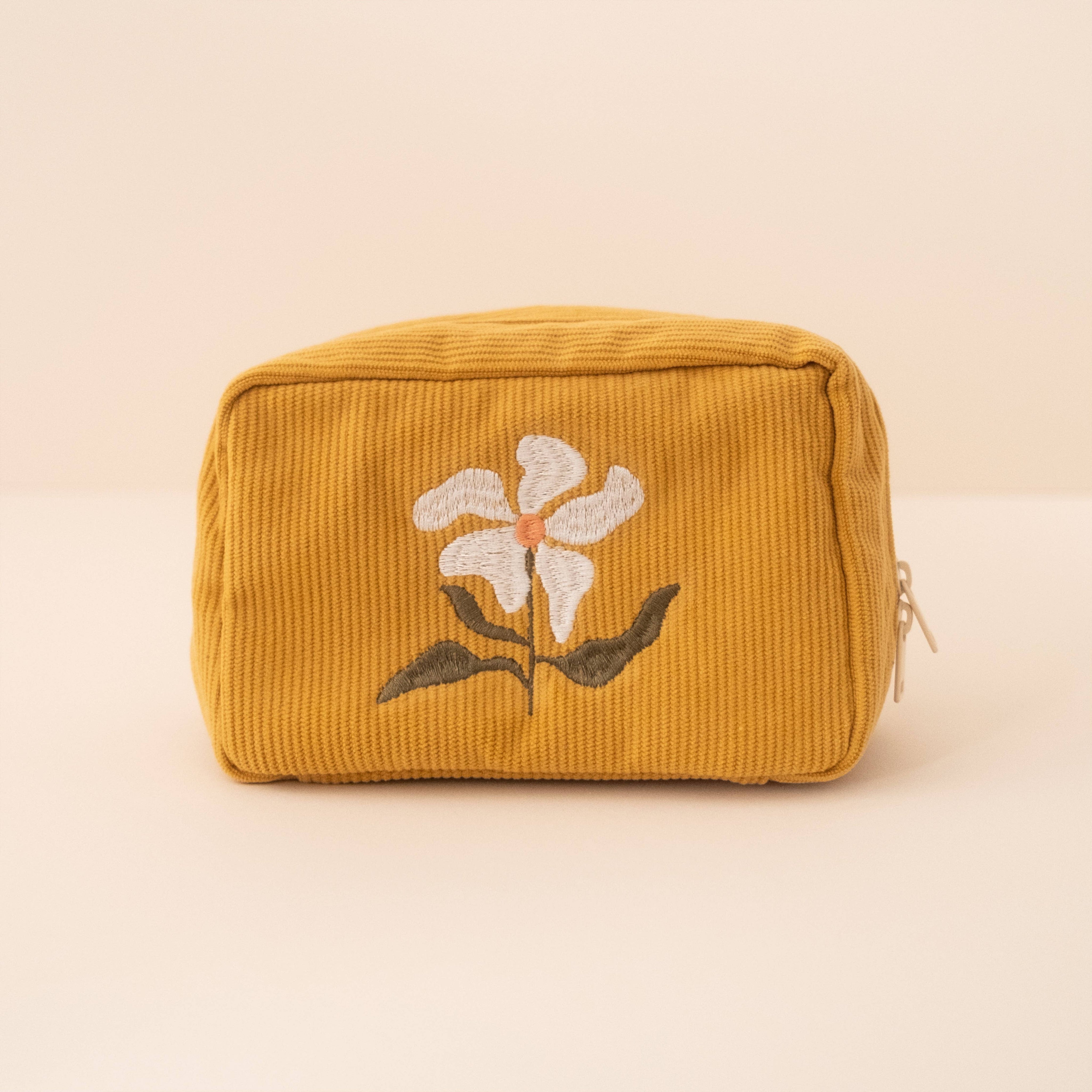 A yellow corduroy makeup bag with a floral embroidery design, featuring a double zip fastening.