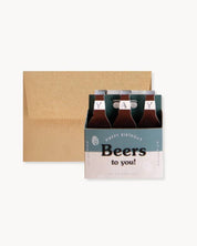 Six-pack of beer with a 'Happy Birthday Beers to you!' card on a white background