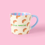 Mug with croissant pattern and 'Good Morning' text by Eleanor Bowmer, on a pink background