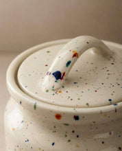 Speckled ceramic jar with a handled lid on a neutral background