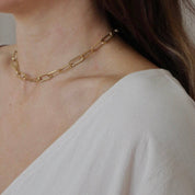 A close-up of a model wearing a delicate gold Buoy chain necklace, paired with a white top.