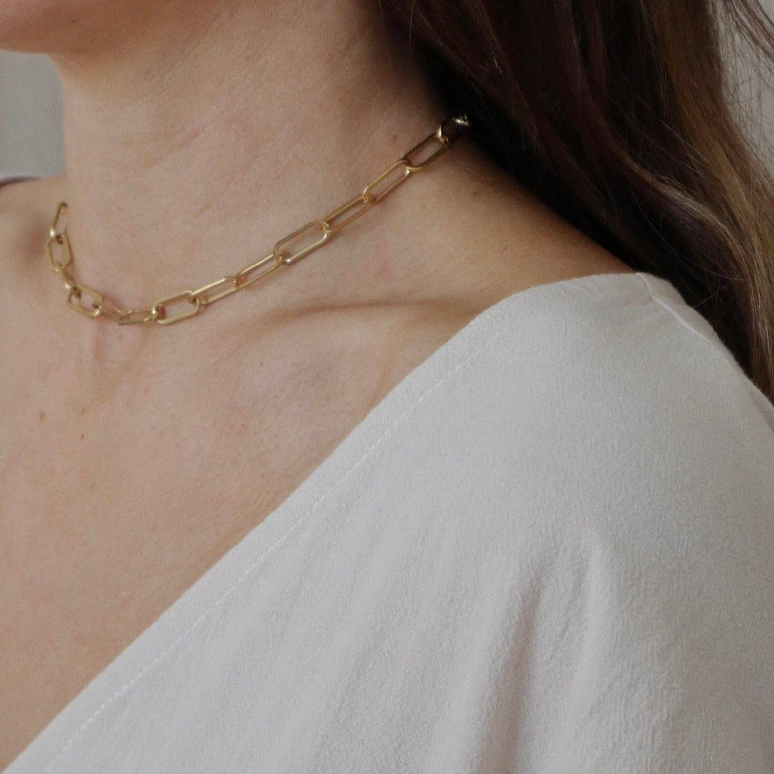 A close-up of a model wearing a delicate gold Buoy chain necklace, paired with a white top.