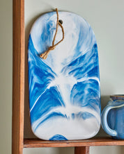 Blue and white marbled cutting board hanging on a wooden shelf.