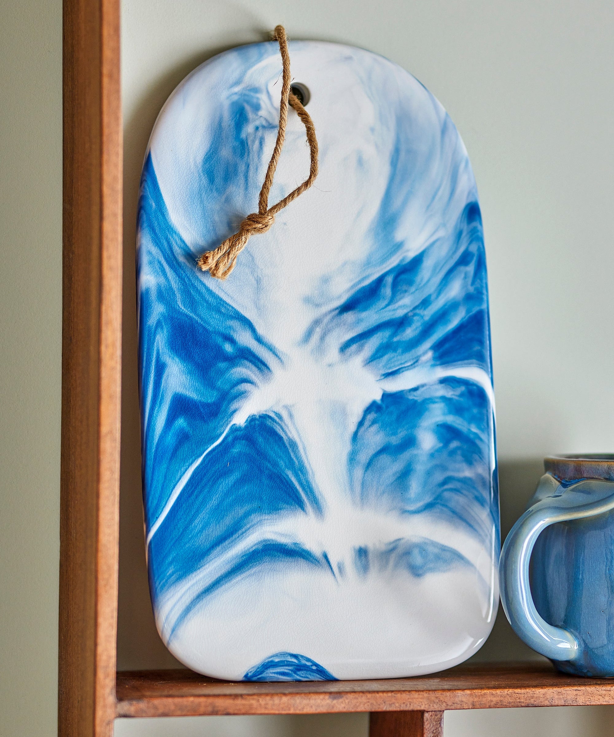 Blue and white marbled cutting board hanging on a wooden shelf.