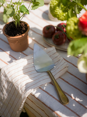 Pie server on a striped tablecloth with potted plants and tomatoes in the background