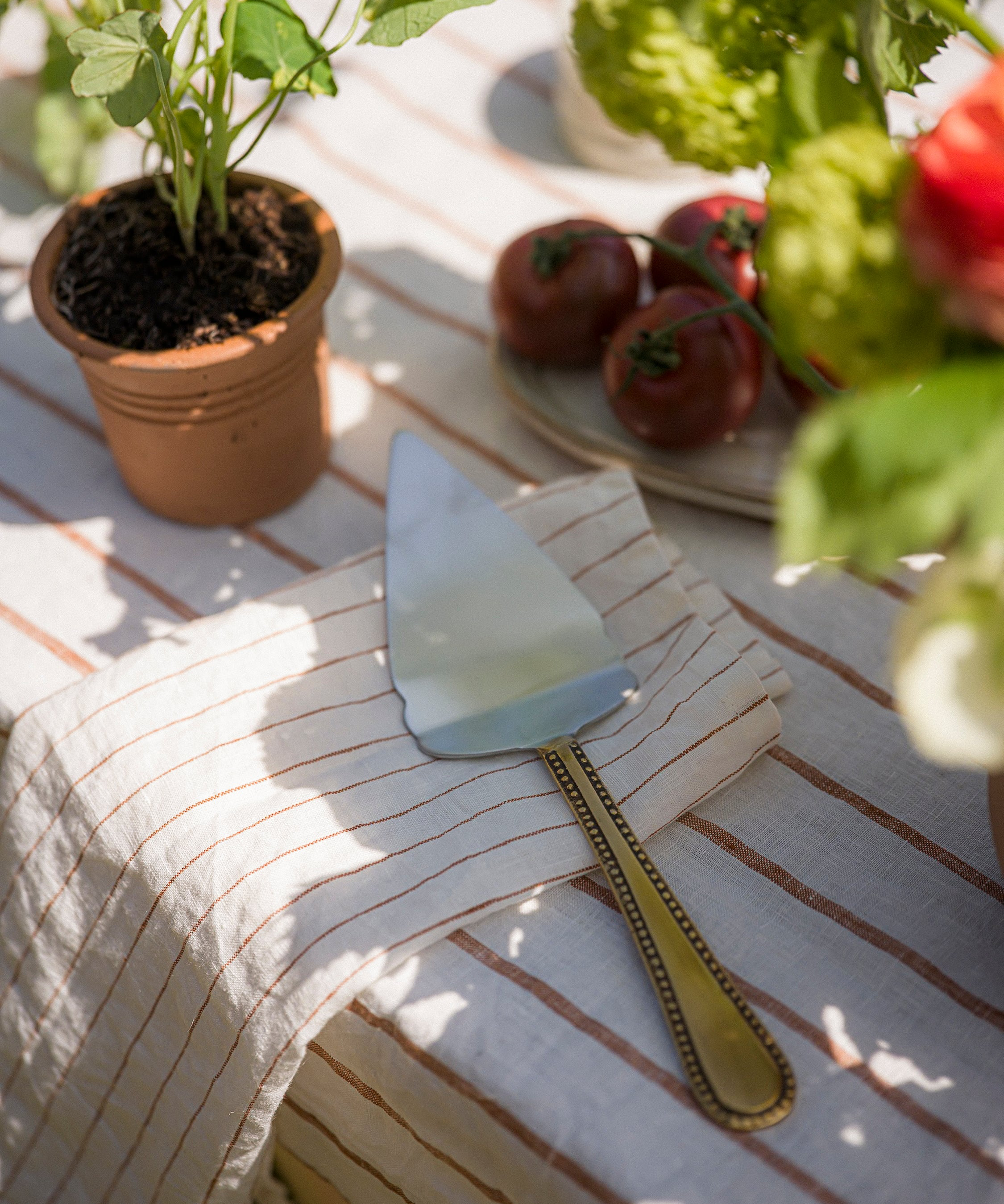 Pie server on a striped tablecloth with potted plants and tomatoes in the background