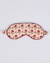 A fabric sleep mask with a light pink background, a repeating dark red rose pattern, and dark red trim, shown on a plain light gray background.