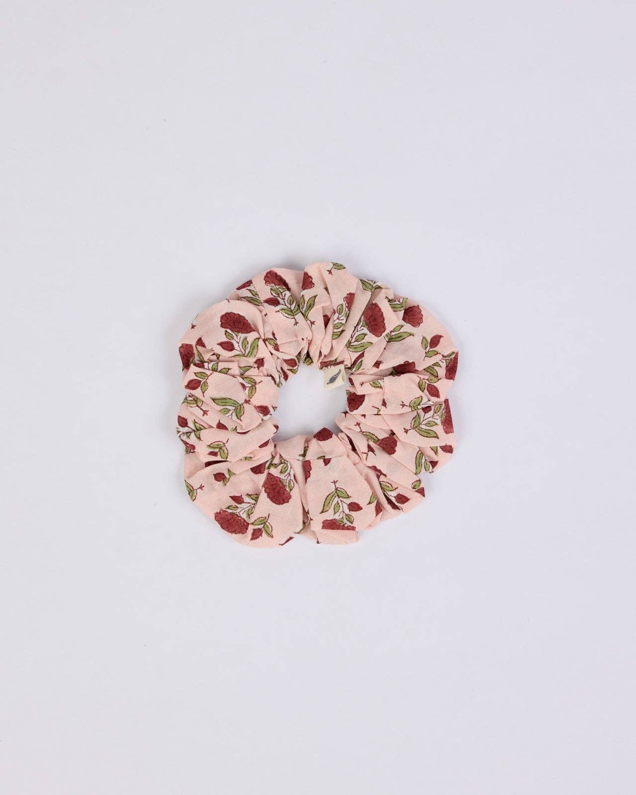 A fabric hair scrunchie with a light pink background and a red berry and green leaf pattern, centered on a plain white background.