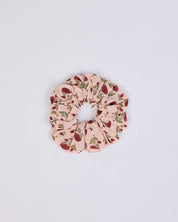 A fabric hair scrunchie with a light pink background and a red berry and green leaf pattern, centered on a plain white background.