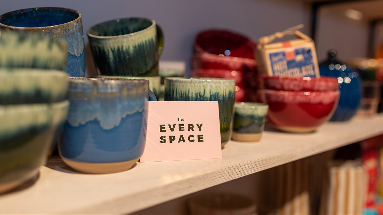 Collection of ceramic cups and bowls on a shelf with 'Every Space' sign.