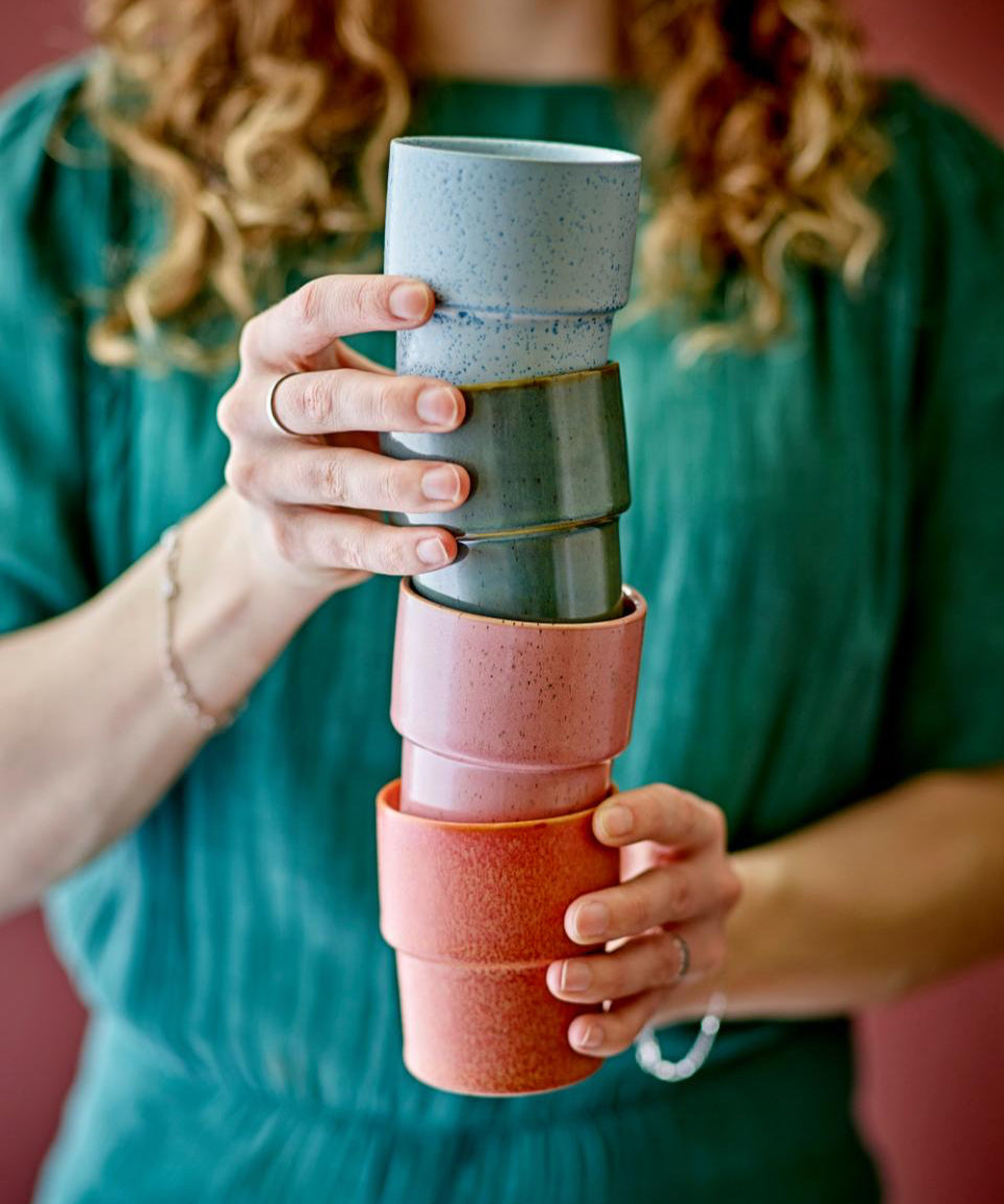 Person holding a stack of colorful ceramic cups against a red background