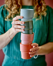 Person holding a stack of colorful ceramic cups against a red background