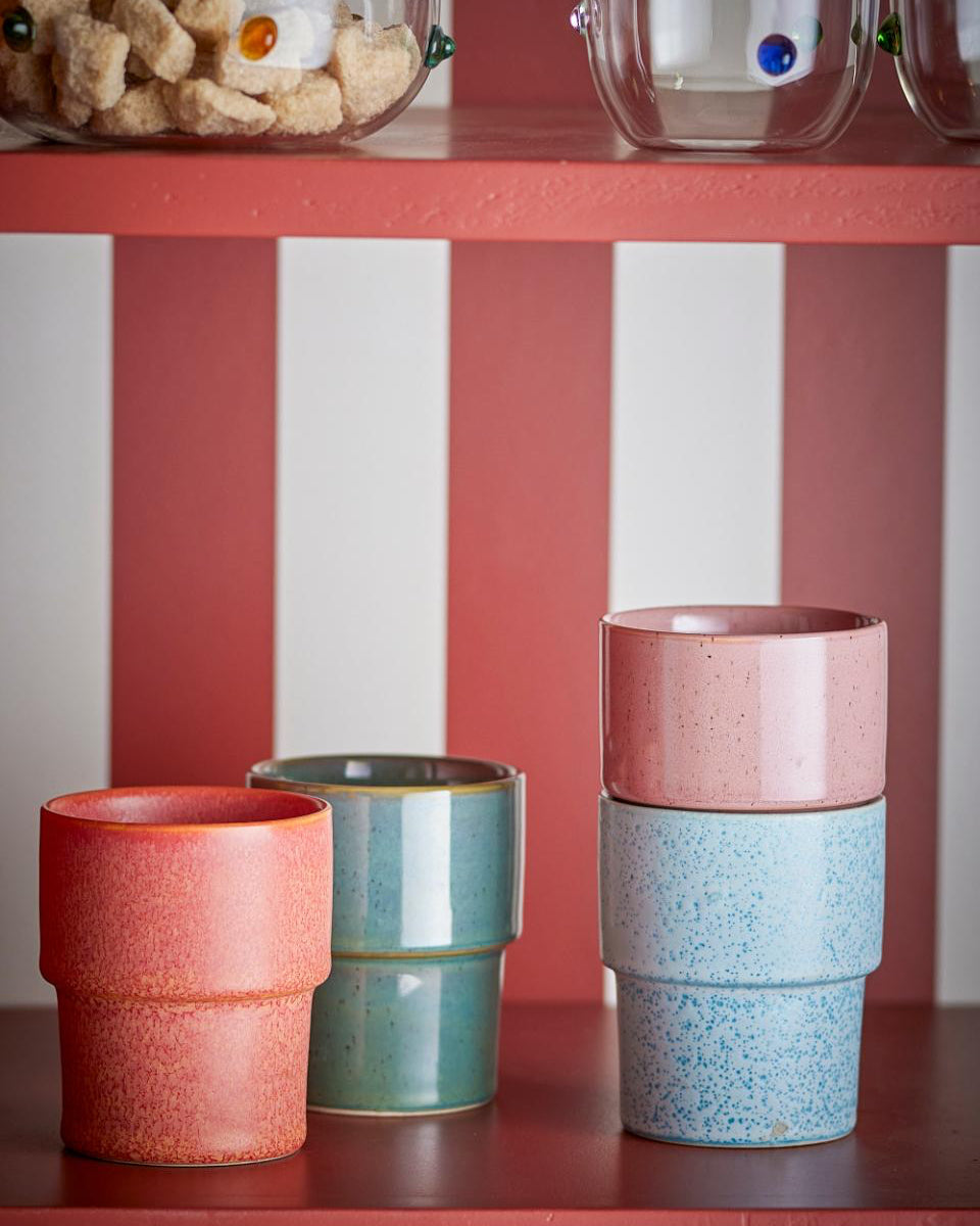 Set of colorful ceramic cups on a red shelf with a striped wall in the background