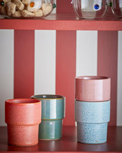 Set of colorful ceramic cups on a red shelf with a striped wall in the background