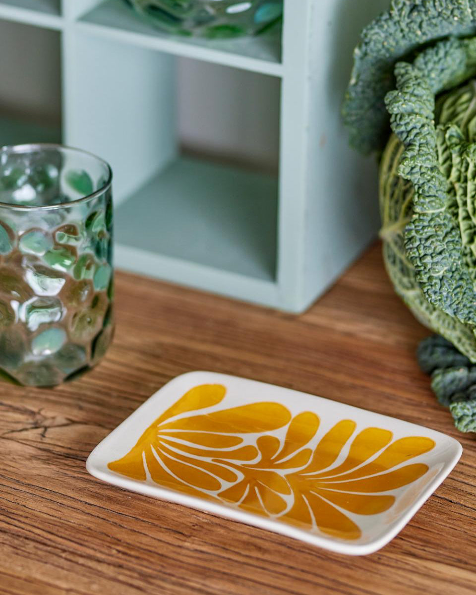 Decorative coaster with yellow floral design on a wooden surface next to a glass and plant.