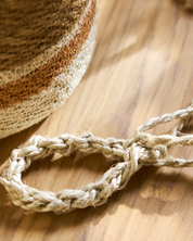 Close-up of a woven bracelet on a wooden surface with a straw hat in the background