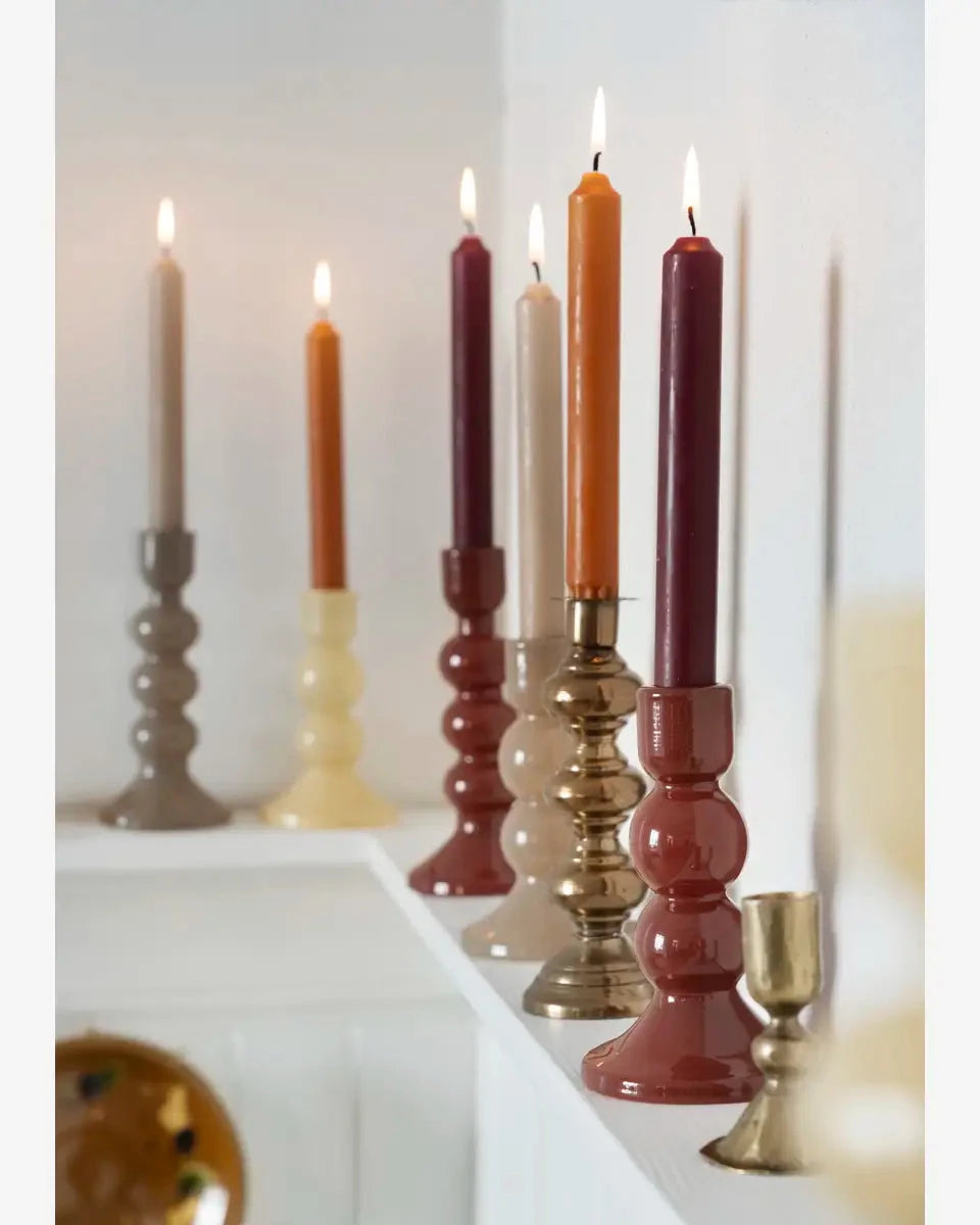 Colorful candles in various holders on a white surface