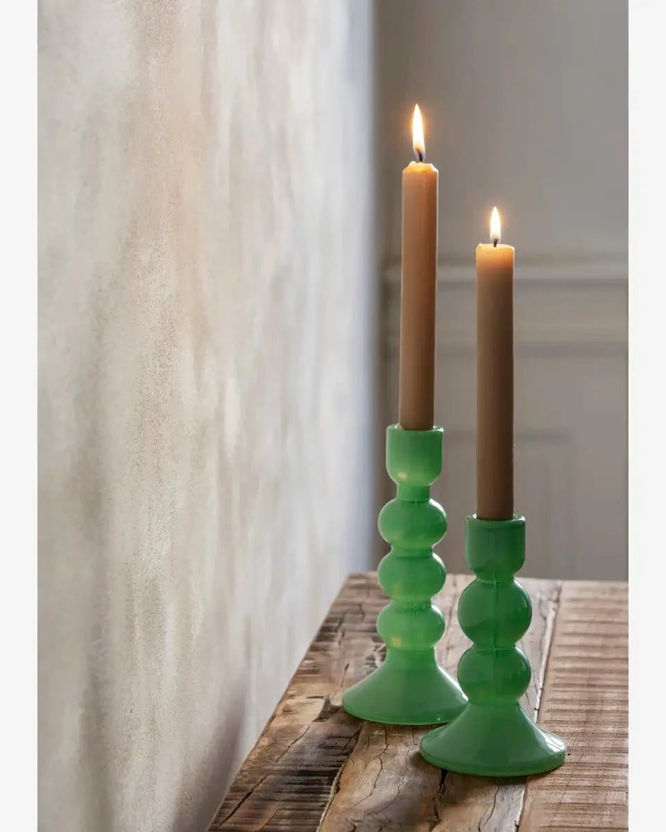 Two green candle holders with lit candles on a wooden surface.