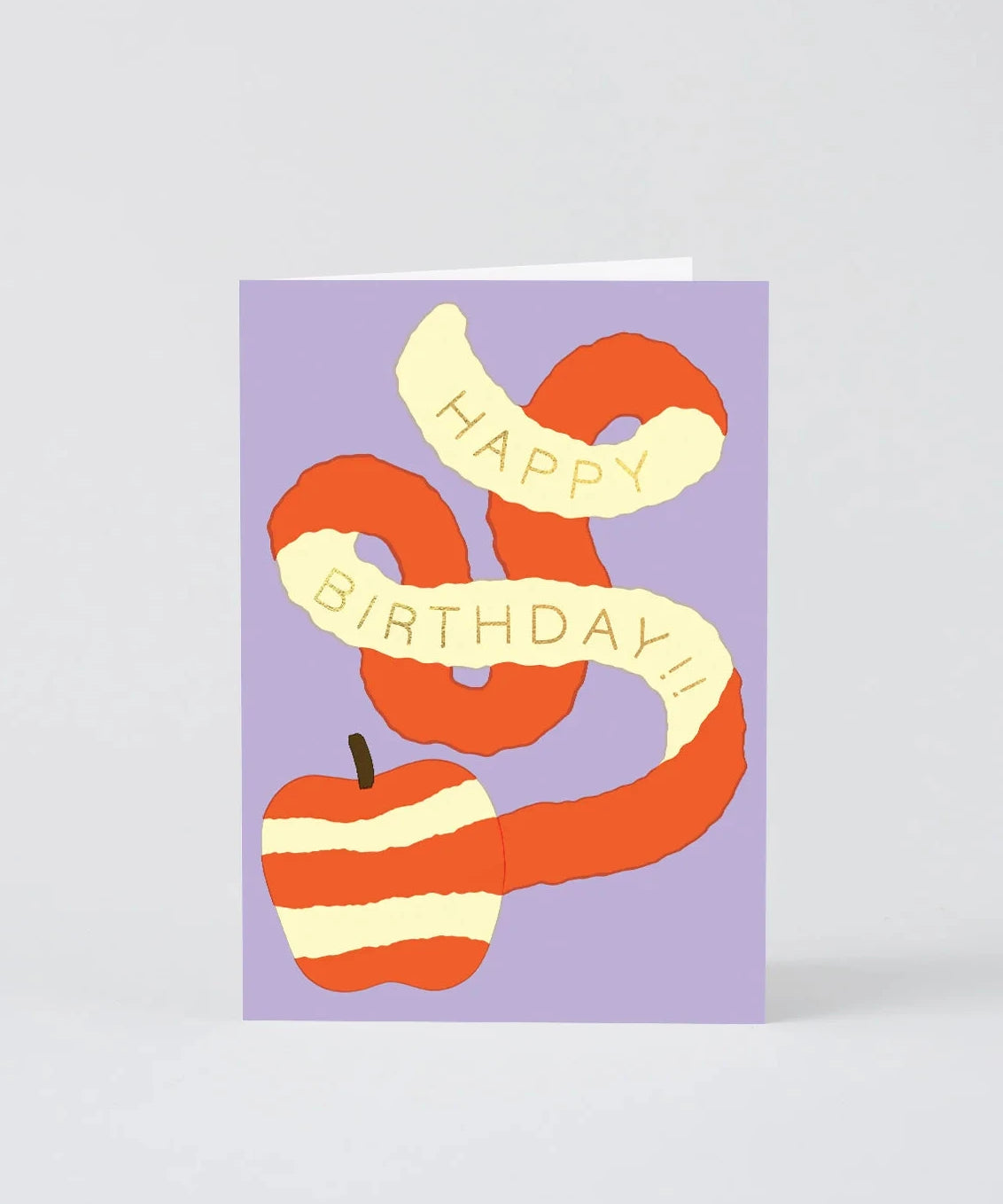 A square birthday greeting card with a lavender background, featuring a stylized orange and cream striped apple and ribbon banner that reads 'HAPPY BIRTHDAY!!' in cream lettering. The card is photographed standing upright on a light gray background.