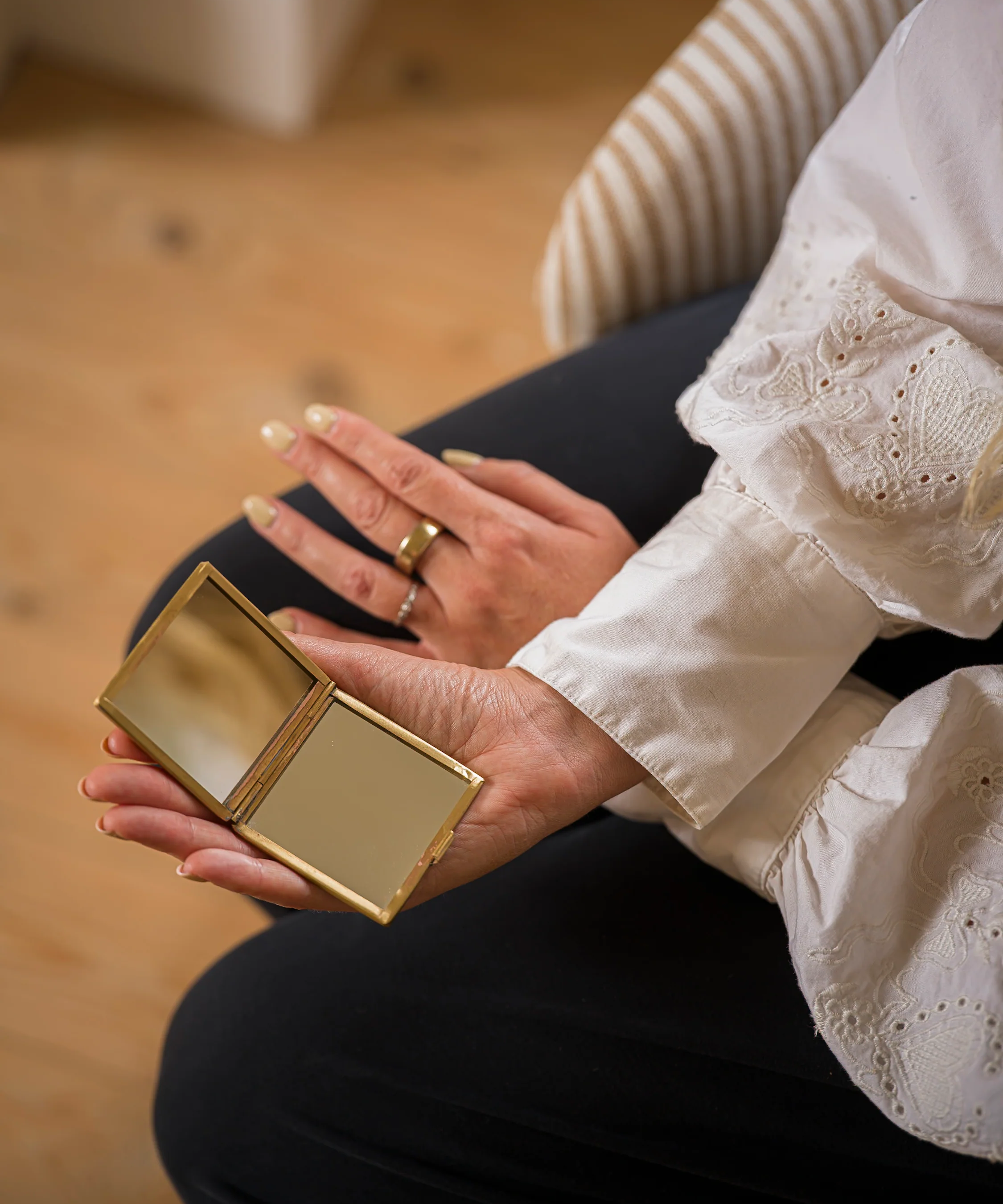 Person holding a gold compact mirror with a blurred background