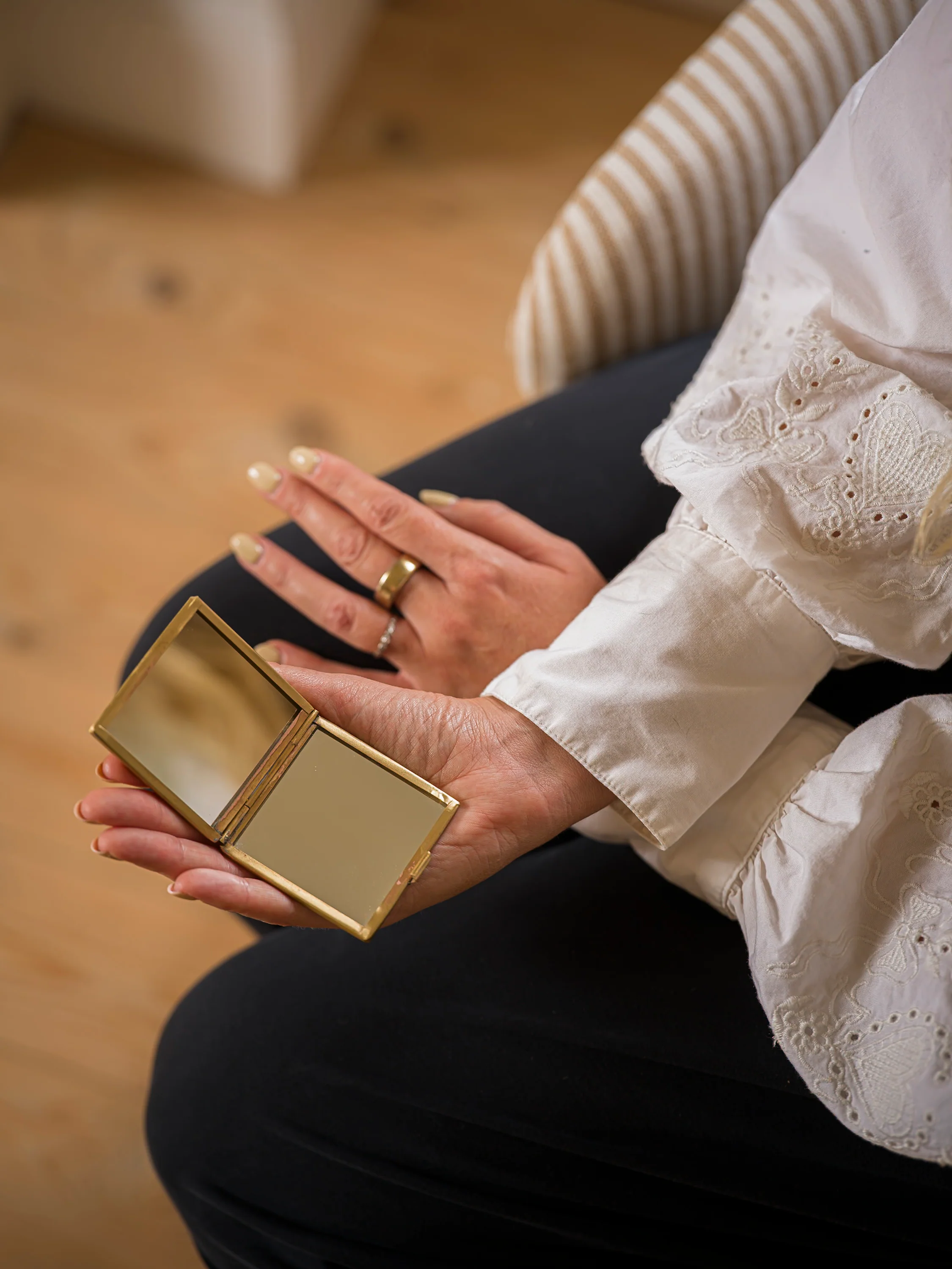 Person holding a gold compact mirror with a blurred background