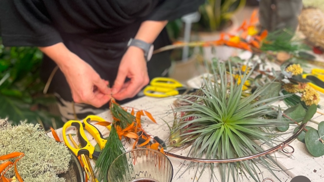 Person working with plants and tools on a table in an outdoor setting