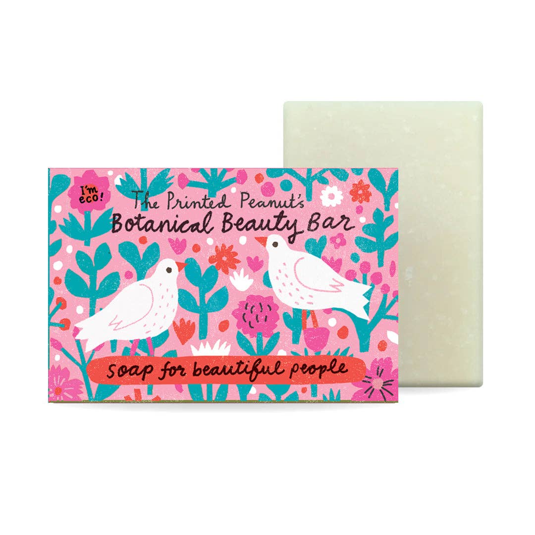 The Printed Peanut's Botanical Beauty Bar soap shown with its colorful illustrated packaging on a white background. The box features pink, teal, and white floral and bird artwork, and the bar of soap behind it is a pale sage green.