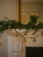 a jingle bell garland with Christmas tree branches on a mantel 