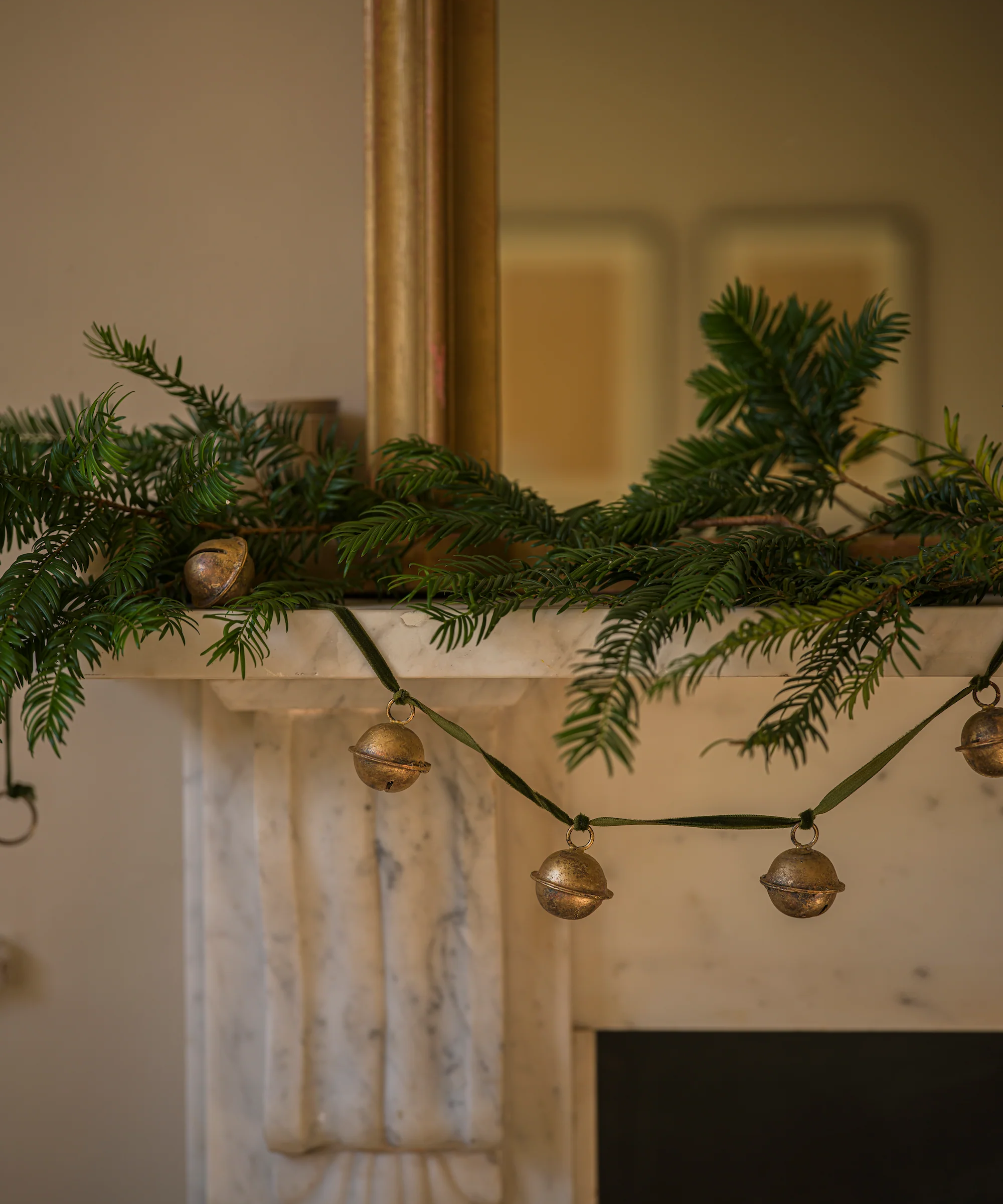 a jingle bell garland with Christmas tree branches on a mantel 