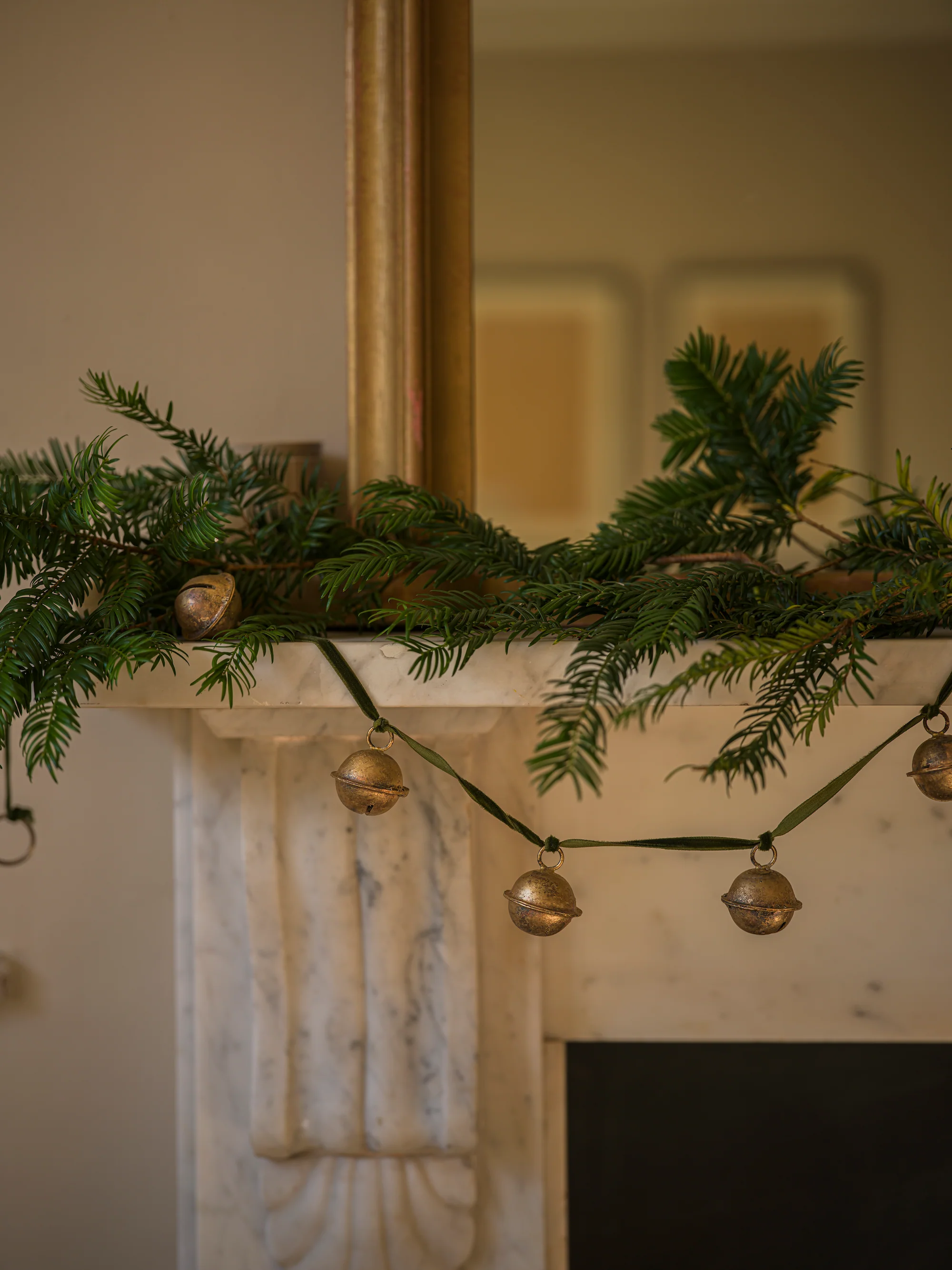 a jingle bell garland with Christmas tree branches on a mantel 