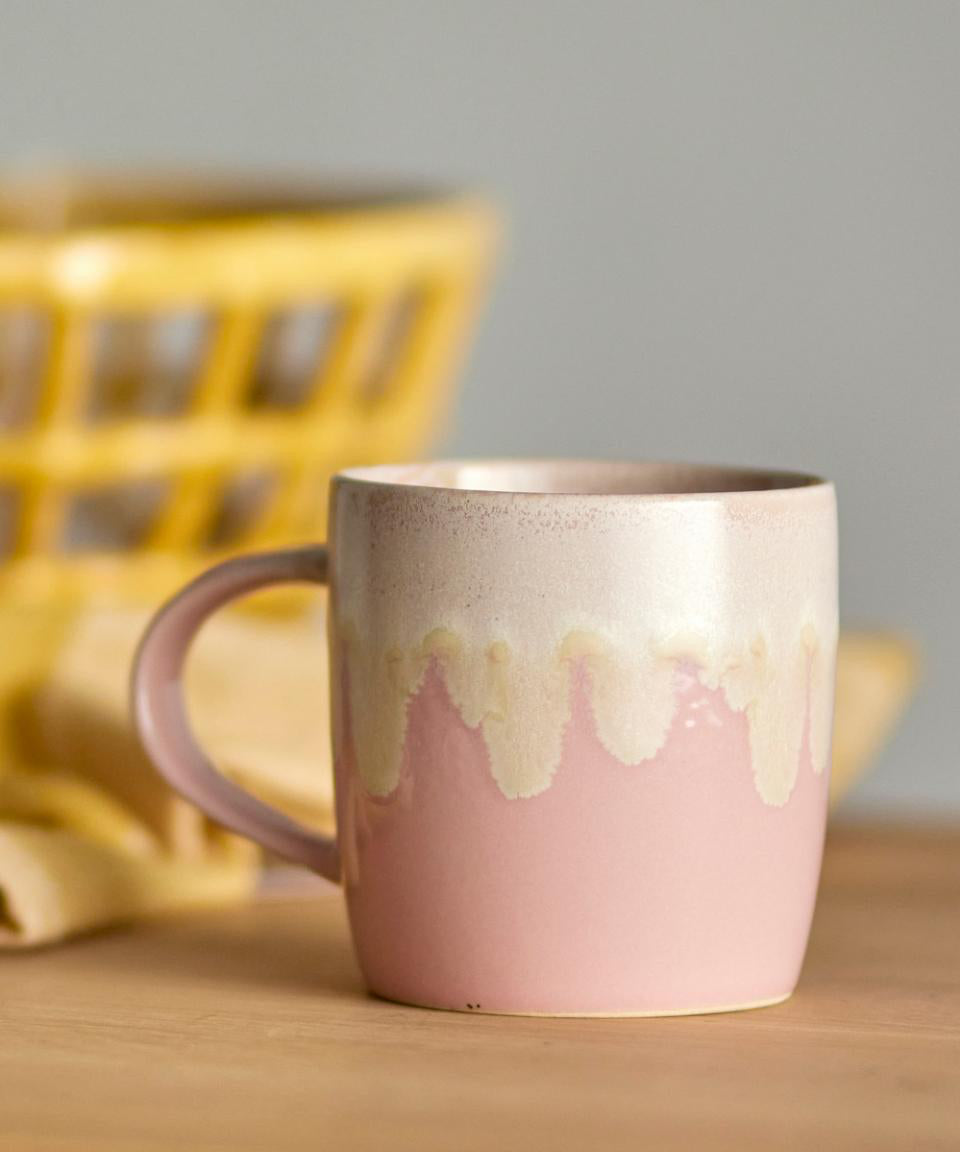 Pink ceramic mug with a textured design on a wooden surface with a blurred yellow basket in the background.
