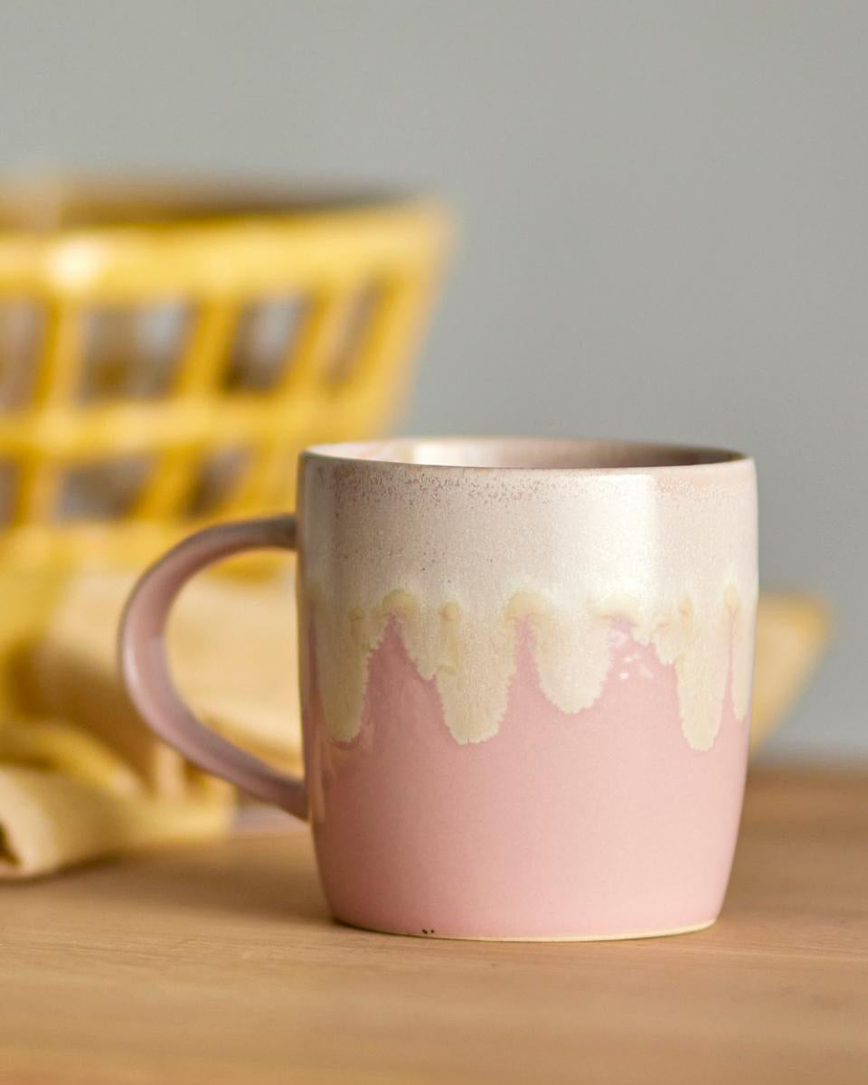 Pink ceramic mug with a textured design on a wooden surface with a blurred yellow basket in the background.
