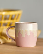 Pink ceramic mug with a textured design on a wooden surface with a blurred yellow basket in the background.