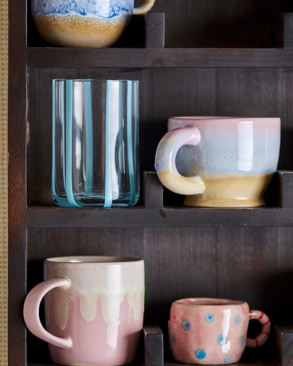 Collection of ceramic mugs with gradient designs on a wooden shelf.